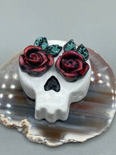 Load image into Gallery viewer, Cremation memorial art, such as Day of the Dead Spirit Pieces, provide a unique way to keep a loved one close to your heart. Handcrafted with care, each piece of artwork is specially tailored to the individual, providing a lasting reminder of those who are dearly missed. On altars and ofrendas, these pieces make a beautiful addition. Composed with meticulous attention to detail, these mini polymer clay skulls feature hand sculpted dark red roses and leaves. H 1 1/2” x W 1 1/2” x D 3/4”