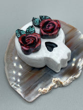 Load image into Gallery viewer, Cremation memorial art, such as Day of the Dead Spirit Pieces, provide a unique way to keep a loved one close to your heart. Handcrafted with care, each piece of artwork is specially tailored to the individual, providing a lasting reminder of those who are dearly missed. On altars and ofrendas, these pieces make a beautiful addition. Composed with meticulous attention to detail, these mini polymer clay skulls feature hand sculpted dark red roses and leaves. H 1 1/2” x W 1 1/2” x D 3/4”