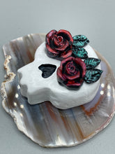 Load image into Gallery viewer, Cremation memorial art, such as Day of the Dead Spirit Pieces, provide a unique way to keep a loved one close to your heart. Handcrafted with care, each piece of artwork is specially tailored to the individual, providing a lasting reminder of those who are dearly missed. On altars and ofrendas, these pieces make a beautiful addition. Composed with meticulous attention to detail, these mini polymer clay skulls feature hand sculpted dark red roses and leaves. H 1 1/2” x W 1 1/2” x D 3/4”