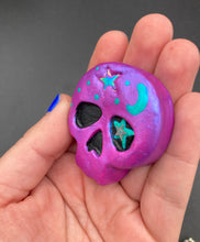 Load image into Gallery viewer, Cute and spooky magnet design to adorn your refrigerator, lockers, workstation, toolbox, or dishwasher. This skull statuette is a tribute to nature. Its metallic violet hue evokes sundown, transitioning the sky from blue to purple to black. Adding to the appeal of this piece is a teal-green moon and stars that provide a dramatic contrast against the violet. The forehead is finished with a rainbow hematite star bead for a unique accent.  H 1 1/2” x W 1 1/2” x D 3/4”