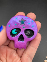 Load image into Gallery viewer, Inspired by nature, this skull statuette is full of shimmery metallic, and vibrant colors and intricate details. The metallic violet color reminds me of sundown, when the sky is illuminating from blue to purple to black. I painted a moon and stars with a teal/green paint to really create a beautiful contrast against the violet color. The forehead of the skully has a beautiful rainbow hematite star bead.