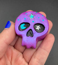 Load image into Gallery viewer, Inspired by nature, this skull statuette is full of shimmery metallic, and vibrant colors and intricate details. The metallic violet color reminds me of sundown, when the sky is illuminating from blue to purple to black. I painted a moon and stars with a teal/green paint to really create a beautiful contrast against the violet color. The forehead of the skully has a beautiful rainbow hematite star bead.