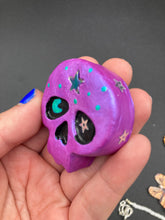 Load image into Gallery viewer, Inspired by nature, this skull statuette is full of shimmery metallic, and vibrant colors and intricate details. The metallic violet color reminds me of sundown, when the sky is illuminating from blue to purple to black. I painted a moon and stars with a teal/green paint to really create a beautiful contrast against the violet color. The forehead of the skully has a beautiful rainbow hematite star bead.