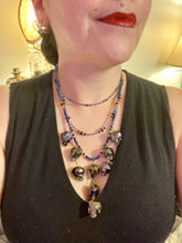 Load image into Gallery viewer, Massively beautiful and bold skull necklace is the ultimate statement piece to add to your jewelry collection! Three strands necklace, contains 5 strands of large skull beads that give a cascade look to this beautiful necklace. Edgy gun metal faceted shimmery multi-color glass hues of silver, purple, pink, blue, and gold. This bold and beautiful necklace drapes across your neck, comes with dainty matching earrings to complete the look. Necklace is 15 1/2” adjustable up to 18" - glass skulls are 5/8”