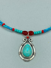 Load image into Gallery viewer, This captivating Southwestern style necklace features a two-strand design of bold and vibrant turquoise and red glass beads. At the center, a bright turquoise pendant is framed in a distinctive design. Measurements: Necklace is 16 1/2 ” adjustable up to 18"