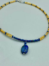 Load image into Gallery viewer, This Lapis pendant necklace features dark blue cats eye beads and two strands of gold glass beads with dark blue double hole beads. The large multi-colored glass beads provide remarkable shimmer and a full range of colors, such as purples, blues, greens, and golds, that enhances the lapis stone pendant. Measurements: Necklace is 19” in length