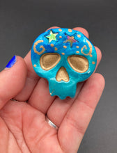 Load image into Gallery viewer, Perfect item to add to your fridge, locker, cubicle, toolbox or dishwasher. This handcrafted skull statuette features shimmering metallic and vivid blue hues, metallic gold stars, and intricate detailing. The skull's forehead is adorned with a glittering hematite star bead.  Measurements: H 1 1/2” x W 1 1/2” x D 3/4”