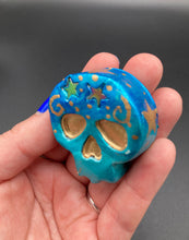 Load image into Gallery viewer, Perfect item to add to your fridge, locker, cubicle, toolbox or dishwasher. This handcrafted skull statuette features shimmering metallic and vivid blue hues, metallic gold stars, and intricate detailing. The skull's forehead is adorned with a glittering hematite star bead.  Measurements: H 1 1/2” x W 1 1/2” x D 3/4”
