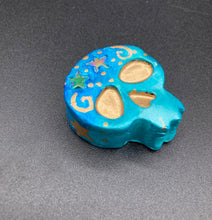 Load image into Gallery viewer, Perfect item to add to your fridge, locker, cubicle, toolbox or dishwasher. This handcrafted skull statuette features shimmering metallic and vivid blue hues, metallic gold stars, and intricate detailing. The skull's forehead is adorned with a glittering hematite star bead.  Measurements: H 1 1/2” x W 1 1/2” x D 3/4”