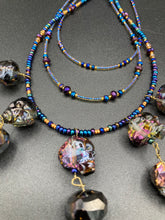Load image into Gallery viewer, Massively beautiful and bold skull necklace is the ultimate statement piece to add to your jewelry collection! Three strands necklace, contains 5 strands of large skull beads that give a cascade look to this beautiful necklace. Edgy gun metal faceted shimmery multi-color glass hues of silver, purple, pink, blue, and gold. This bold and beautiful necklace drapes across your neck, comes with dainty matching earrings to complete the look. Necklace is 15 1/2” adjustable up to 18" - glass skulls are 5/8”