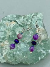 Load image into Gallery viewer, These elegant, glass beaded earrings feature dainty light and dark purple hues, making them a great addition to any summer wardrobe. Perfect for hippie and nature-inspired looks, they are sure to accentuate any style.  Measurements: 1 ” in length