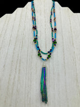Load image into Gallery viewer, This Celestial and Galaxy Vibe Necklace features a 2 1/2" long Rainbow Kyanite Wired Stone pendant and two strands of multi-color glass beaded necklaces. The glass beads are an eclectic mix of sizes and shapes, including rectangular hematite beads, creating a shimmery, bold display of purples, blues, greens and golds. This necklace truly captures the essence of this celestial galaxy stone.Necklace is 15 1/2” in length can be adjusted to 18" in length