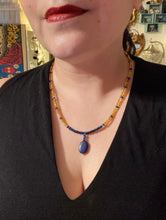 Load image into Gallery viewer, This Lapis pendant necklace features dark blue cats eye beads and two strands of gold glass beads with dark blue double hole beads. The large multi-colored glass beads provide remarkable shimmer and a full range of colors, such as purples, blues, greens, and golds, that enhances the lapis stone pendant. Measurements: Necklace is 19” in length