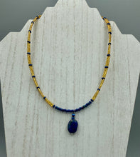 Load image into Gallery viewer, This Lapis pendant necklace features dark blue cats eye beads and two strands of gold glass beads with dark blue double hole beads. The large multi-colored glass beads provide remarkable shimmer and a full range of colors, such as purples, blues, greens, and golds, that enhances the lapis stone pendant. Measurements: Necklace is 19” in length