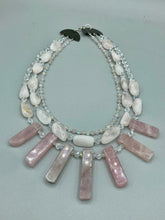 Load image into Gallery viewer, This impressive three-strand necklace is crafted from natural rose quartz stones and iridescent glass beads. The shortest strand is composed of petite round rose quartz beads, while the second strand contains an array of rectangular-shaped rose quartz and iridescent glass beads. The longest strand has long, vertical rectangular-shaped rose quartz beads, creating an elegant display across the chest. This necklace is an impressive, dynamic accessory. Necklace is 17: in length, can be adjusted to 19"