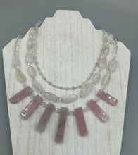 Load image into Gallery viewer, This impressive three-strand necklace is crafted from natural rose quartz stones and iridescent glass beads. The shortest strand is composed of petite round rose quartz beads, while the second strand contains an array of rectangular-shaped rose quartz and iridescent glass beads. The longest strand has long, vertical rectangular-shaped rose quartz beads, creating an elegant display across the chest. This necklace is an impressive, dynamic accessory. Necklace is 17: in length, can be adjusted to 19"