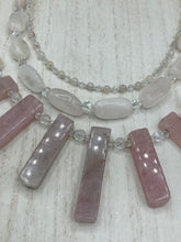 Load image into Gallery viewer, This impressive three-strand necklace is crafted from natural rose quartz stones and iridescent glass beads. The shortest strand is composed of petite round rose quartz beads, while the second strand contains an array of rectangular-shaped rose quartz and iridescent glass beads. The longest strand has long, vertical rectangular-shaped rose quartz beads, creating an elegant display across the chest. This necklace is an impressive, dynamic accessory. Necklace is 17: in length, can be adjusted to 19"