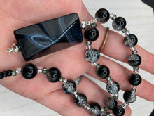 Load image into Gallery viewer, This black agate natural stone necklace features a unique rectangular pyramid shape and multi-colored glass beads. Perfect for all kinds of looks, from cocktail attire to shabby chic to elegant goth styles, this necklace is as versatile as it is stylish and will complete any outfit. The set includes matching earrings, making it a must-have addition to any jewelry collection. Measurements: Necklace is 18 1/2”