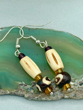 Load image into Gallery viewer, This set of earrings features a cylinder bone bead and round bone bead with eye design and a gold-tone glass bead. Neutral colors allow for versatile styling; the resulting look is sure to be unique.  Measurements: 1 1/2 ” in length