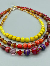 Load image into Gallery viewer, This necklace consists of three strands with a multitude of shades ranging from red to orange, gold, and amber, providing a captivating visual combination. Crafted with a combination of glass, ceramic and metal beads, this eye-catching piece of jewelry radiates power and strength. Measurements: Necklace is 16” in length, can be adjusted up to 17 1/2"