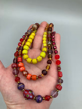 Load image into Gallery viewer, This necklace consists of three strands with a multitude of shades ranging from red to orange, gold, and amber, providing a captivating visual combination. Crafted with a combination of glass, ceramic and metal beads, this eye-catching piece of jewelry radiates power and strength. Measurements: Necklace is 16” in length, can be adjusted up to 17 1/2"