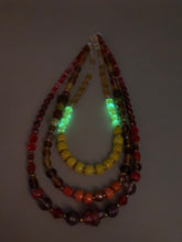 Load image into Gallery viewer, This necklace consists of three strands with a multitude of shades ranging from red to orange, gold, and amber, providing a captivating visual combination. Crafted with a combination of glass, ceramic and metal beads, this eye-catching piece of jewelry radiates power and strength. Measurements: Necklace is 16” in length, can be adjusted up to 17 1/2"
