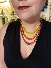 Load image into Gallery viewer, This necklace consists of three strands with a multitude of shades ranging from red to orange, gold, and amber, providing a captivating visual combination. Crafted with a combination of glass, ceramic and metal beads, this eye-catching piece of jewelry radiates power and strength. Measurements: Necklace is 16” in length, can be adjusted up to 17 1/2"