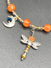 Load image into Gallery viewer, This bright orange, adjustable, choker-style necklace is adorned with beaded glass and a striking crescent moon charm and dragonfly pendant. Accessorize with matching dragonfly earrings for an eye-catching, complementary look that captures the warmth of summer. Perfect for any outfit, its vibrant colors will make a statement and complete any look. Measurements: Necklace is 16 1/2”adjustable up to 19"