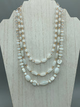 Load image into Gallery viewer, This necklace is the perfect finishing touch to any outfit. Featuring three strands of white and gold glass beads for a classic and elegant look. The small clear and gold glass beads add a touch of sophistication. Adjustable for a comfortable fit. Measurements: Necklace is 17” in length, can be adjusted up to 19 1/2"