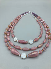 Load image into Gallery viewer, This three-strand beaded necklace is crafted with iridescent dusty rose glass, along with white, gold, pink, and iridescent purple beads for an eclectic mix of colors, tones, and textures. Perfect for any occasion, this gorgeous statement piece will add the finishing touch to your look. Measurements: Necklace is 17” in length, can be adjusted up to 19"