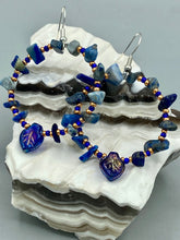 Load image into Gallery viewer, Featuring natural lapis stone chips and royal blue glass beads with golden accents, these hoop earrings complete any look with a dark blue pressed glass leaf charm boasting an iridescent shimmer with hints of gold, purple, blue and pink. Measurements: 1 3/4" length