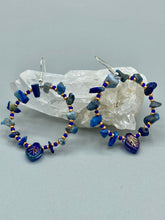 Load image into Gallery viewer, Featuring natural lapis stone chips and royal blue glass beads with golden accents, these hoop earrings complete any look with a dark blue pressed glass leaf charm boasting an iridescent shimmer with hints of gold, purple, blue and pink. Measurements: 1 3/4" length