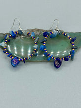 Load image into Gallery viewer, Featuring natural lapis stone chips and royal blue glass beads with golden accents, these hoop earrings complete any look with a dark blue pressed glass leaf charm boasting an iridescent shimmer with hints of gold, purple, blue and pink. Measurements: 1 3/4" length