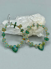 Load image into Gallery viewer, Natural aventurine stone chips, turquoise, and gold glass beads are strung together to form these stylish hoop earrings. The dark green pressed glass leaf charm complements the design, creating an iridescent, shimmery finish with subtle hues of gold, purple, blue, and pink. Measurements: 2" length