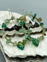 Load image into Gallery viewer, Natural aventurine stone chips, turquoise, and gold glass beads are strung together to form these stylish hoop earrings. The dark green pressed glass leaf charm complements the design, creating an iridescent, shimmery finish with subtle hues of gold, purple, blue, and pink. Measurements: 2" length