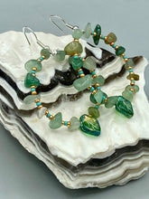 Load image into Gallery viewer, Natural aventurine stone chips, turquoise, and gold glass beads are strung together to form these stylish hoop earrings. The dark green pressed glass leaf charm complements the design, creating an iridescent, shimmery finish with subtle hues of gold, purple, blue, and pink. Measurements: 2" length