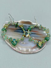 Load image into Gallery viewer, Natural aventurine stone chips, turquoise, and gold glass beads are strung together to form these stylish hoop earrings. The dark green pressed glass leaf charm complements the design, creating an iridescent, shimmery finish with subtle hues of gold, purple, blue, and pink. Measurements: 2" length