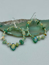 Load image into Gallery viewer, Natural aventurine stone chips, turquoise, and gold glass beads are strung together to form these stylish hoop earrings. The dark green pressed glass leaf charm complements the design, creating an iridescent, shimmery finish with subtle hues of gold, purple, blue, and pink. Measurements: 2" length