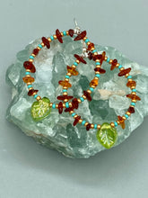 Load image into Gallery viewer, These Amber Stone Chip Beaded Hoop Earrings feature turquoise and gold glass beads, and a light green glass leaf charm with an iridescent shimmer finish with hints of gold, purple, blue, and pink. Measurements: 2" length