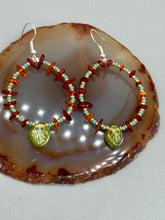 Load image into Gallery viewer, These Amber Stone Chip Beaded Hoop Earrings feature turquoise and gold glass beads, and a light green glass leaf charm with an iridescent shimmer finish with hints of gold, purple, blue, and pink. Measurements: 2" length