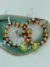 Load image into Gallery viewer, These Amber Stone Chip Beaded Hoop Earrings feature turquoise and gold glass beads, and a light green glass leaf charm with an iridescent shimmer finish with hints of gold, purple, blue, and pink. Measurements: 2" length