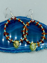 Load image into Gallery viewer, These Amber Stone Chip Beaded Hoop Earrings feature turquoise and gold glass beads, and a light green glass leaf charm with an iridescent shimmer finish with hints of gold, purple, blue, and pink. Measurements: 2" length