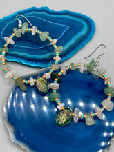 Load image into Gallery viewer, These handmade hoop earrings feature natural Aventurine and White Moon Stone chips along with turquoise and gold glass beads. The light green-toned pressed glass leaf charm beautifully shimmers with iridescent hues of gold, purple, blue, and pink. Measurements: 2" length