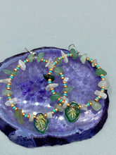 Load image into Gallery viewer, These handmade hoop earrings feature natural Aventurine and White Moon Stone chips along with turquoise and gold glass beads. The light green-toned pressed glass leaf charm beautifully shimmers with iridescent hues of gold, purple, blue, and pink. Measurements: 2" length