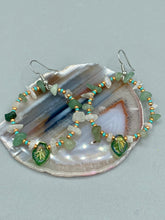 Load image into Gallery viewer, These handmade hoop earrings feature natural Aventurine and White Moon Stone chips along with turquoise and gold glass beads. The light green-toned pressed glass leaf charm beautifully shimmers with iridescent hues of gold, purple, blue, and pink. Measurements: 2" length
