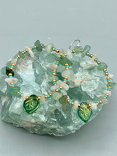 Load image into Gallery viewer, These handmade hoop earrings feature natural Aventurine and White Moon Stone chips along with turquoise and gold glass beads. The light green-toned pressed glass leaf charm beautifully shimmers with iridescent hues of gold, purple, blue, and pink. Measurements: 2" length