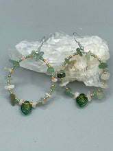Load image into Gallery viewer, These handmade hoop earrings feature natural Aventurine and White Moon Stone chips along with turquoise and gold glass beads. The light green-toned pressed glass leaf charm beautifully shimmers with iridescent hues of gold, purple, blue, and pink. Measurements: 2" length