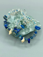 Load image into Gallery viewer, These earrings boast a beautiful combination of natural lapis and white moon stone chip stones, artfully inlaid with gold glass beads in a hoop formation. Dainty conch shells add a subtle touch of nature for a look that perfectly captures the beach vibes of summer. An ideal choice to complement any style. Measurements: 2 1/4" length