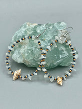 Load image into Gallery viewer, Dainty conch shells and natural white moon stone chips, these dark silver and gold glass beaded hoop earrings are the perfect accessory for any nature-loving, beach-themed outfit. Their versatility allows them to easily complement any outfit. Measurements: 2 1/4" length
