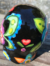 Load image into Gallery viewer, This hand-painted ceramic skull art is an homage to the traditional Mexican Day of the Dead. The inspiration for the skull's exquisite detail was taken from a beautiful flower photographed at the United States Botanic Garden - a whimsical surprise of small flowers floating in water. Bring La Muerte Calavera de Ofrenda, or 'skull of offering', into your home for a captivating reminder of Mexican tradition. H 2 3/4” x W 2” x D 2”